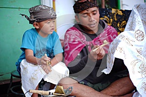 A father is teaching his son to make batik
