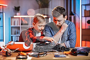 Father teaching his son to repair red toy car