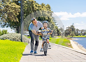 Father teaching his son to ride a bike and having fun together at the park