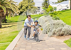 Father teaching his son to ride a bike and having fun together at the park