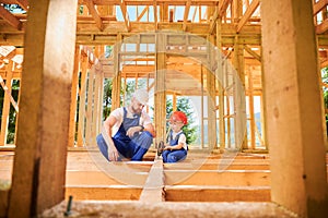 Father teaching his toddler son the art building wooden frame house on construction site.