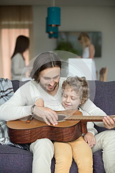 Father teaching son play guitar, family leisure activity at home