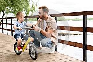 father teaching son riding bike on bridge