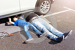 Father teaching son to repair car lying under auto