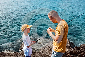 Father teaching young son fishing in the sea. Standing on rock, coast together holding fish rod. Top view.