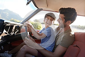 Father Teaching Young Son To Drive Car On Road Trip