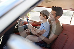 Father Teaching Young Son To Drive Car On Road Trip