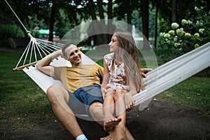 Father and teen daughter relaxing on a hammock in the woods. Happy family sitting together in park. Outdoors relaxation.