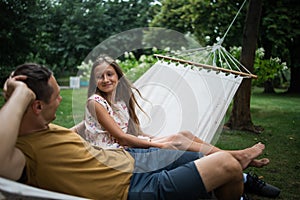 Father and teen daughter relaxing on a hammock in the woods. Happy family sitting together in park. Outdoors relaxation.
