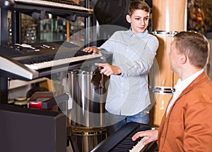 Father and teenage son examining keyboards in guitar shop