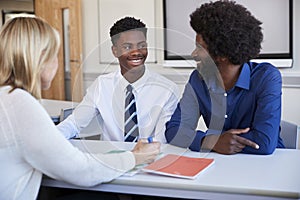 Father And Teenage Son Having Discussion With Female Teacher At High School Parents Evening