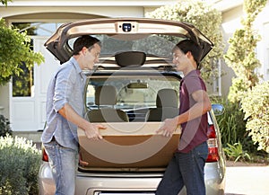 Father And Teenage Son Loading Large Package Into Back Of Car