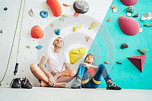 Father and teenage son sitting near the indoor climbing wall. They resting after the active climbing. Happy parenting concept