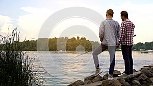 Father and teenager son fishing together, relaxing near lake, favorite hobby