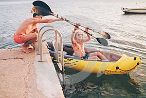 Father with teenager son preparing evening ride loading oars in an inflatable kayak. Adriatic sea harbor in Croatia near from