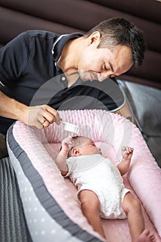 Father tenderly looks at his baby daughter while combing her hair with a brush