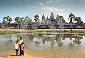 Father with three kids standing past historical landscape of Angkor What temple, 12th century Khmer landmark
