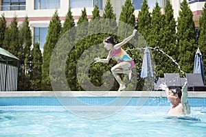 Father throwing daughter into the pool, mid-air