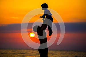 Father throwing his kid up in the air on the beach, silhouette shot