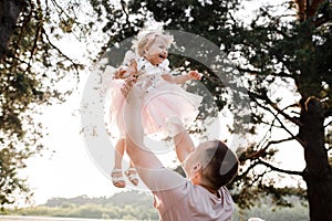 Father throws baby in nature, girl flies in the sky. Portrait dad with child together. Daddy, little daughter outdoors
