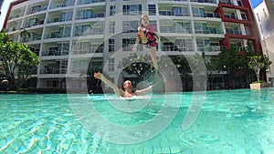 Father throws his daughter in the swimming pool. Slow motion video