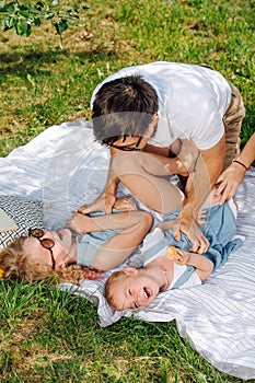 Father tickles his daughters during picnic on grass in the gardens