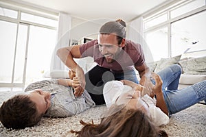 Father Tickling Children As They Play Game In Lounge Together