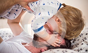 Father with a toddler boy having fun in bedroom at home at bedtime.