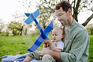 Father and toddler playing with foam glider plane. Single dad having fun with baby during warm spring day. Father& x27;s