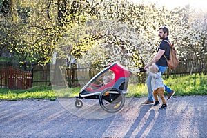 A father with toddler son pushing a jogging stroller outside in spring nature.