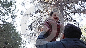 Father tosses the baby up in front of the trees. View from below