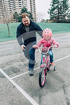 Father training helping girl daughter to ride bicycle.