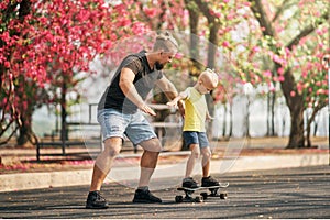 Father training his son to ride a skateboard in park on spring time