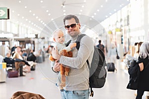 Father traveling with child, holding his infant baby boy at airport terminal waiting to board a plane. Travel with kids