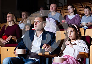 Father and tween daughter watching film together in cinema