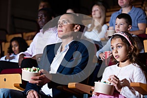 Father and tween daughter watching film together in cinema