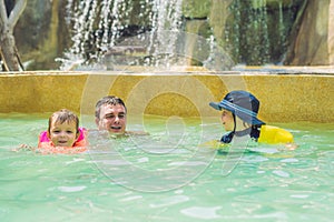 Father and two boys swim in the pool. Happy family playing in blue water of swimming pool on a tropical resort at the sea