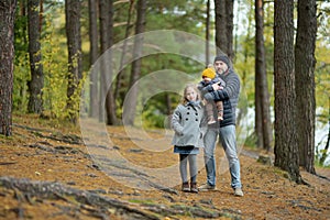 Father and two children having fun on late autumn day by the lake. Adorable baby boy being held by his daddy. Older sister hugging