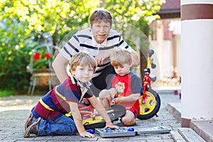 Father and two little sibling boys reparing broken bicycle