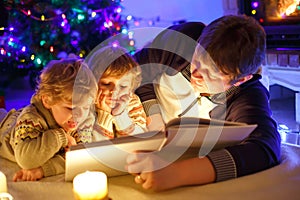 Father and two little toddler boys reading book by chimney, candles and fireplace.