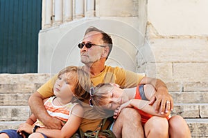 Father with two tired kids resting outside