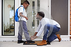 Father Tying Sons Shoelaces As He Leaves For School photo