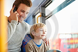 Father Using Mobile Phone On Bus Journey With Son