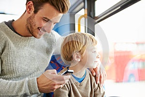 Father Using Mobile Phone On Bus Journey With Son