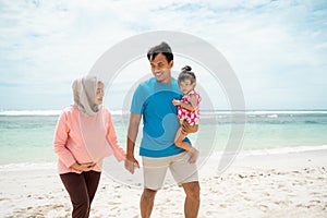 Father walking hold wife hand and carrying his daughter on the beach