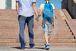 the father walks with his son up the stairs to the school