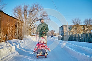 Father walks with a small daughter in a winter village, sledging