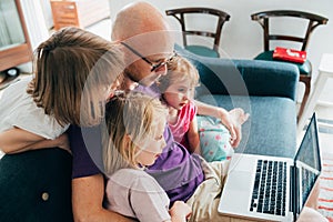 Father watching streaming film on computer with three daughters indoor at home