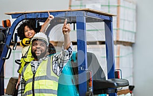 Father wearing safety hard hat, pointing, teaching children to drive tractor in factory to support his work as worker, playing,