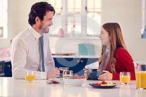 Father Wearing Suit Having Breakfast With Teenage Daughter In School Uniform At Home In Kitchen